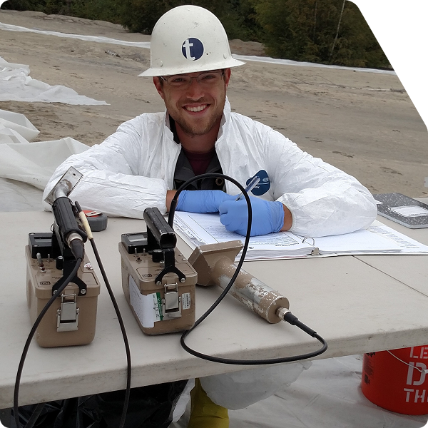 Terraphase worker kneeling in front of table taking notes and smiling at camera.