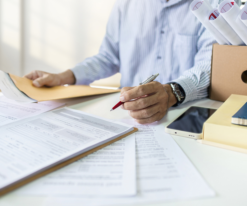 Businessman in office with many documents spread out on desk.