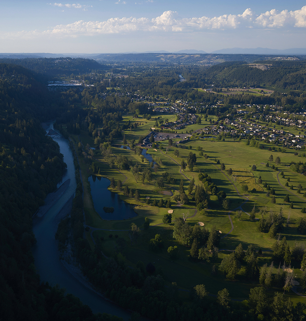 Aerial view of the Puyallup river flowing through a valley with residential houses in the distance.