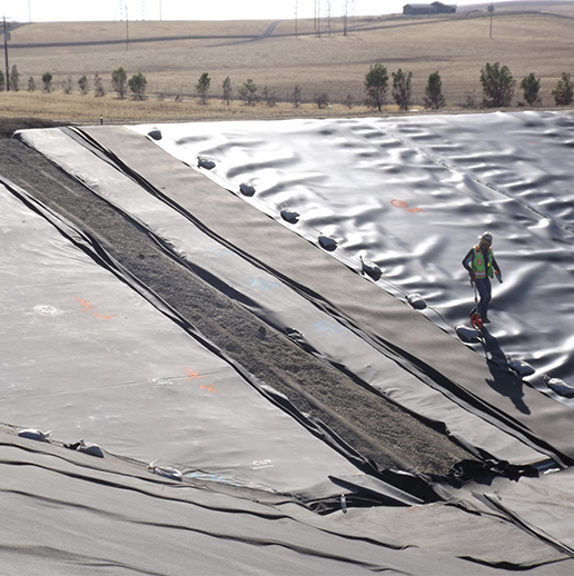 Worker in safety gear walking down lined retention pond.