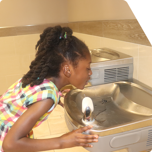 Young school age girl drinking from indoor water fountain.