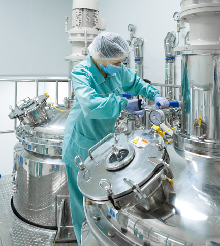 Pharmaceutical factory worker in protective clothing operating production line in sterile environment.