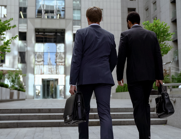 Lawyers approaching office building dressed in suits carrying briefcases.