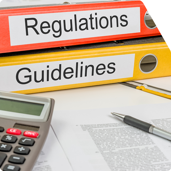 Folders on a table labeled Regulations and Guidelines on top of papers with a pen and calculator