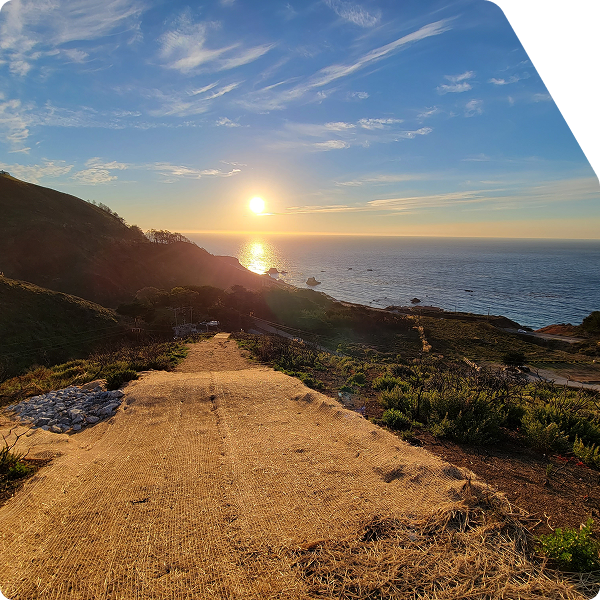 View of erosion control matting with hill and ocean in background at sunset