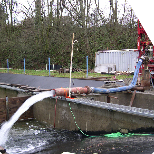 Drill rig with hose extending to spillway where water is being discharged.