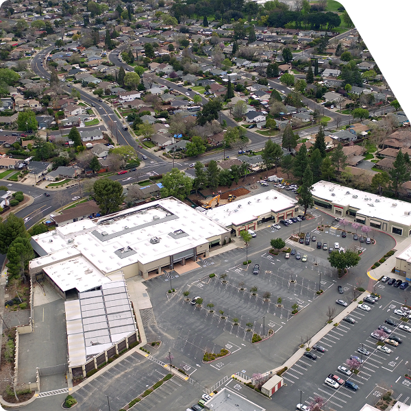 Aerial view of commercial shopping center with adjacent residential neighborhood in the background.