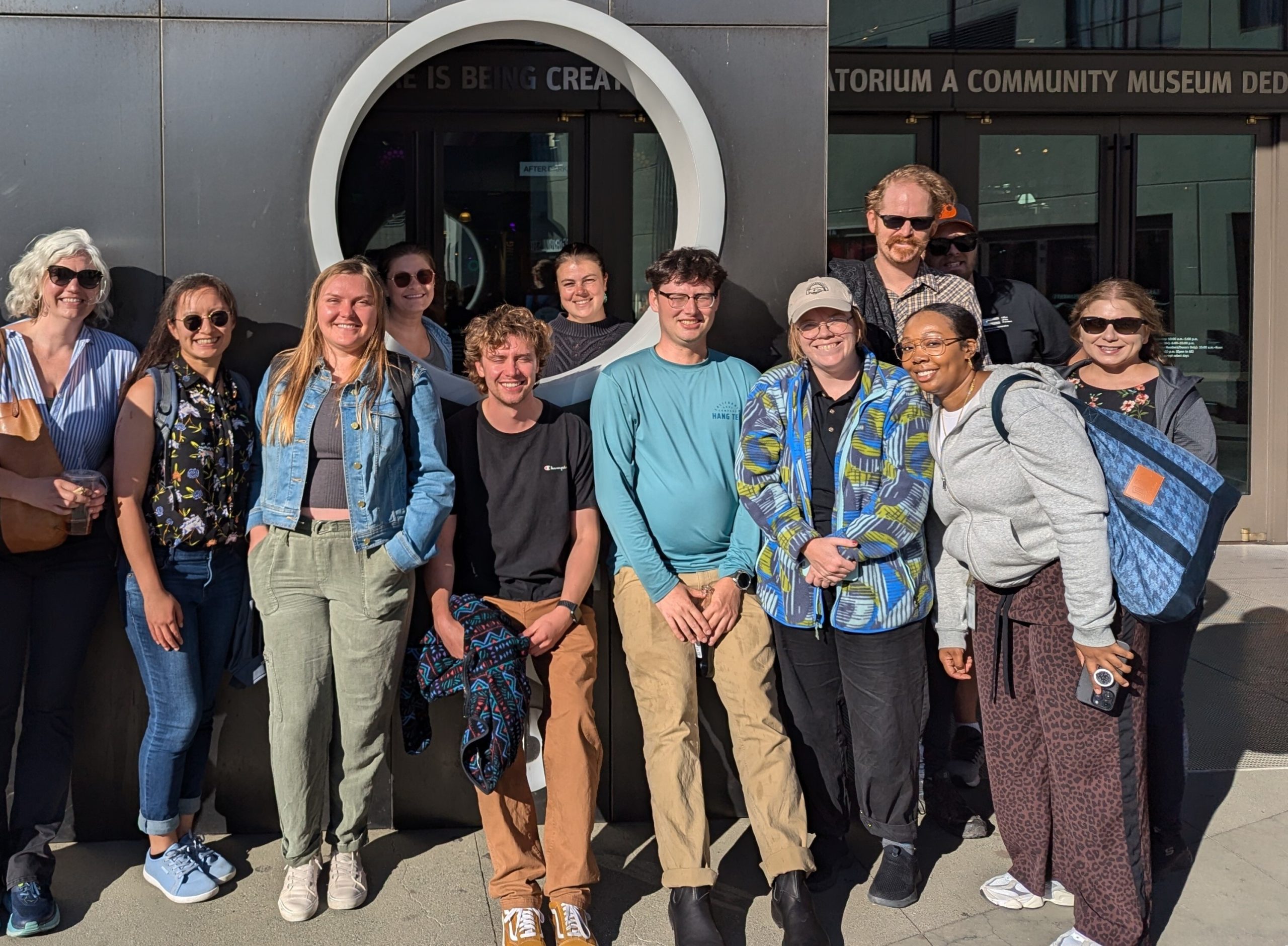 A group of employees posing for a picture in front of a museum.